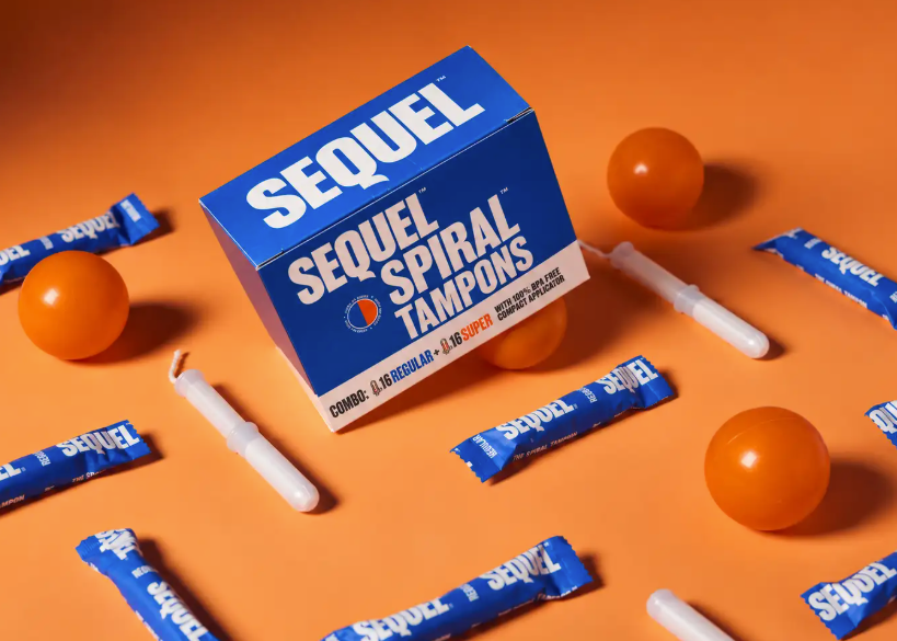 A box of Sequel Spiral Tampons surrounded by individual tampon packets, white tampons, and orange balls on a solid orange background.